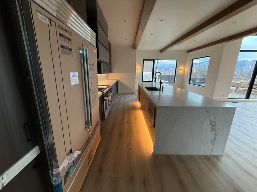 Modern kitchen featuring a sleek marble island, stainless steel appliances, and large windows.